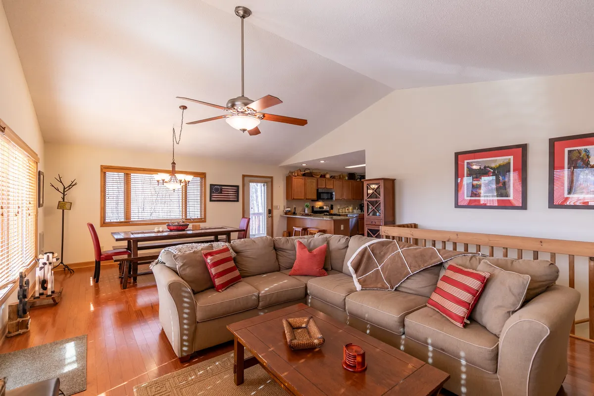 A spacious sectional sofa dominates the foreground, with a dining table and kitchen area visible in the background. The open flow between the living, dining, and kitchen areas is highlighted, showing comfort and ample seating for family activities.
