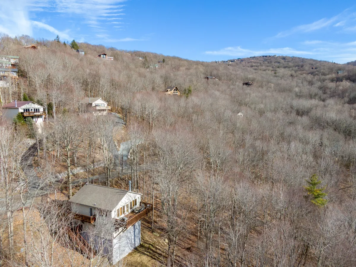 A tranquil exterior scene featuring a single home in the foreground surrounded by lush trees and rolling hills in the distance. The peaceful landscape evokes the tranquility of the High Country and hints at opportunities for hiking, wildlife viewing, and family gatherings in nature.