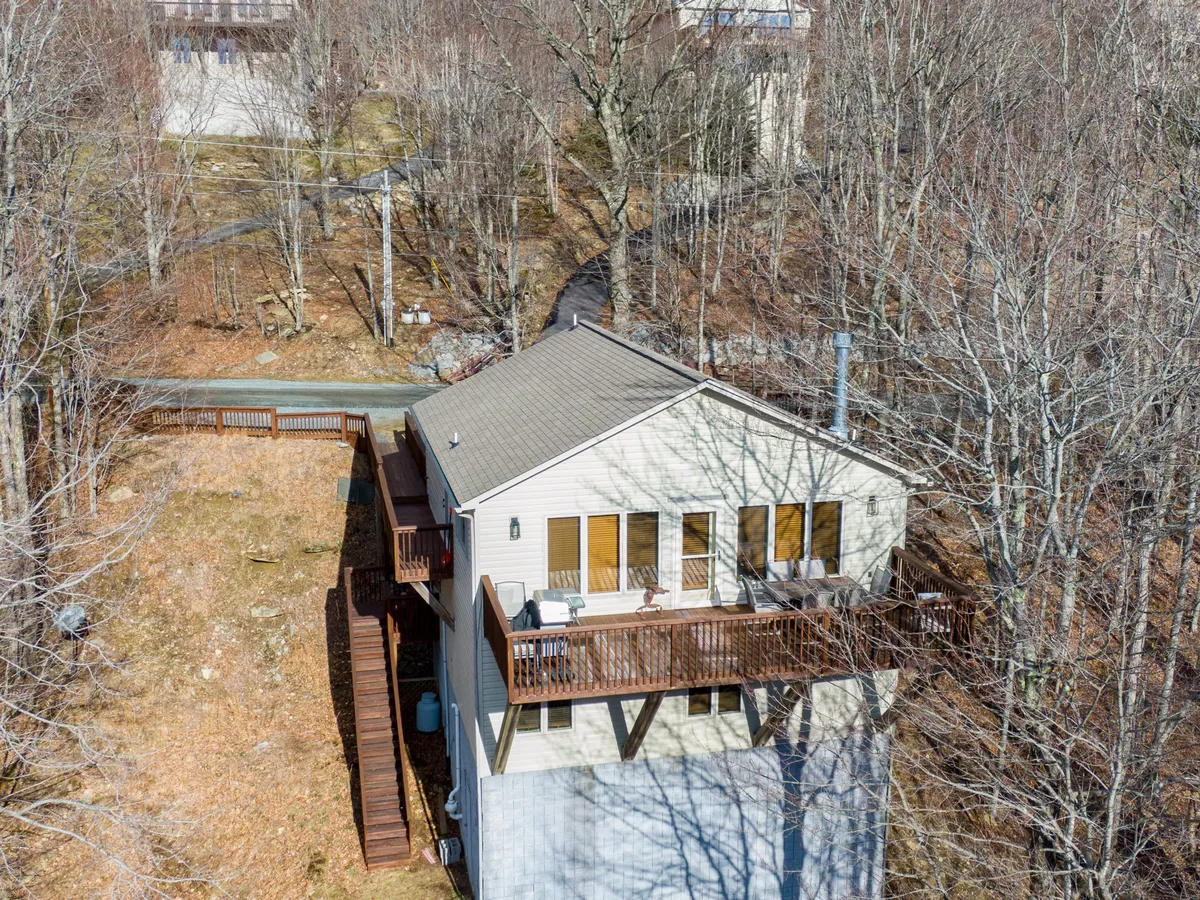 The image displays the house nestled among trees, with the wooden deck clearly visible. The surrounding nature highlights the direct access to the yard and the peaceful, fresh mountain setting described in the section.
