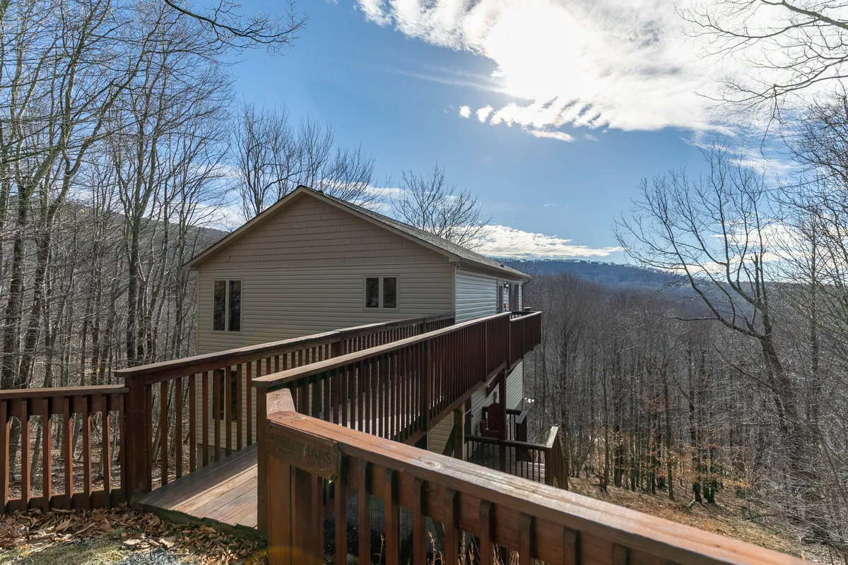 An inviting view of a wooden deck attached to the house, with the home's exterior visible and distant mountains stretching across the background. The deck suggests a serene space for enjoying the fresh air, with the possibility for wildlife observation or stargazing.