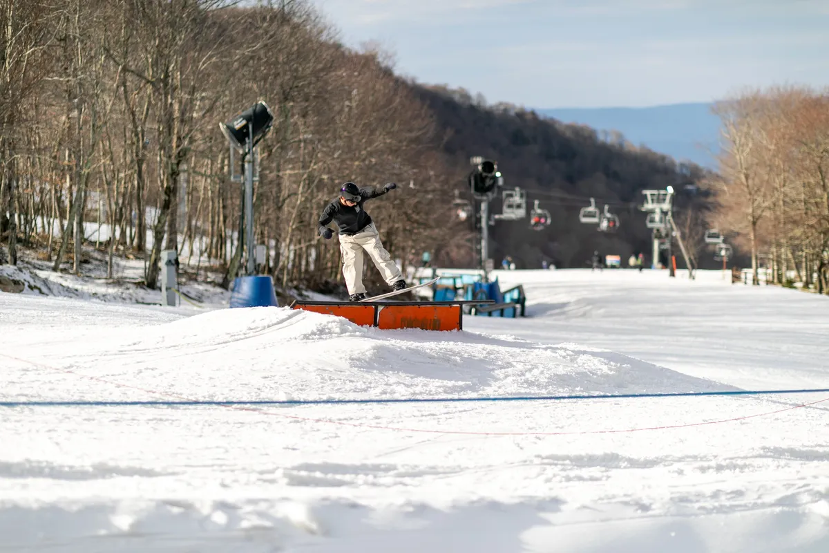 An exterior scene captures a snowboarder performing a trick on snow-covered terrain, with a ski lift and mountain landscape in the background. The image conveys a lively, adventurous atmosphere and hints at the variety of outdoor activities available nearby.