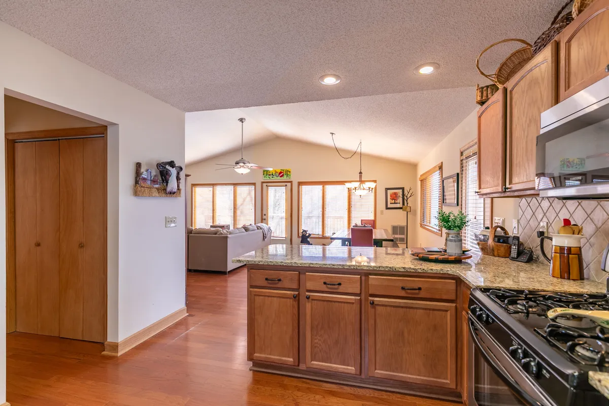 This image features a spacious kitchen island set against large windows that frame glimpses of the outdoors. The living area is visible, suggesting an open-concept space ideal for cooking, socializing, and casual gatherings. The abundance of natural light and the view outside hint at the scenic mountain surroundings that can be enjoyed from within the home.