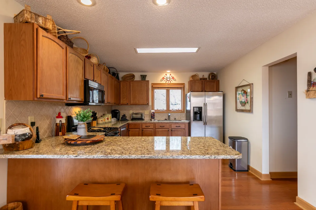 The kitchen is center stage with granite countertops, wooden cabinets, a kitchen island, and a window letting in natural light. The space feels welcoming and ideal for meal preparation and casual gatherings.