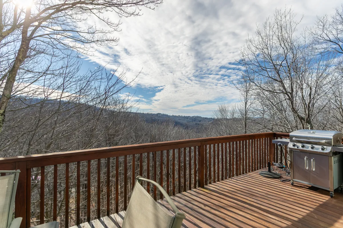This image showcases a spacious wooden deck complete with a grill and comfortable seating, set against a backdrop of sweeping mountain views and tall trees. The deck is bathed in natural light, inviting relaxation and social gatherings while highlighting the seamless connection between the home and the outdoors.